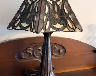 Tiffany-style table lamp features a distinctive pyramidal shade with a stained glass pattern and a molded bronze-tone base