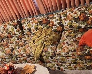 Vintage 1970s Earth-Tone Floral Print 3-Cushion Sofa: Classic 1970s retro couch upholstered in a vibrant earth-tone floral tapestry print (rust, gold, olive, cream) with matching throw pillows and skirted base.