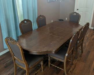 This premium 7-piece Ashley Furniture "Chateau Frontenac" formal dining set includes a large double-pedestal table with removable extension leaves and six upholstered high-back chairs, all beautifully adorned with intricate acanthus leaf and rope-twist carvings