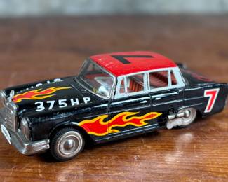 This lot features a vintage Ichiko Japan tin friction Mercedes-Benz toy car from the 1960s. It features a black body with distinctive red and yellow flame decals on the sides and hood.