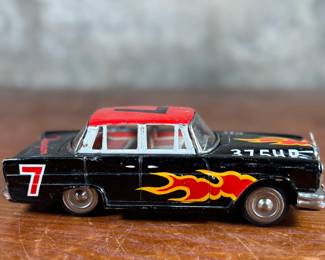 This lot features a vintage Ichiko Japan tin friction Mercedes-Benz toy car from the 1960s. It features a black body with distinctive red and yellow flame decals on the sides and hood.
