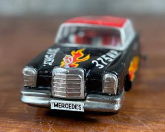 This lot features a vintage Ichiko Japan tin friction Mercedes-Benz toy car from the 1960s. It features a black body with distinctive red and yellow flame decals on the sides and hood.