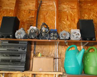 A stereo, some motors and some watering cans, on some shelves