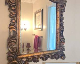 gold and brown carved wood accent mirror from the Howard Elliott Collection featuring a heavily detailed scroll and crest top.    