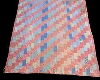 vintage handmade patchwork quilt features a traditional diagonal scrappy design in a mix of faded red, soft blue, and assorted patterned cotton prints. "Trip Around the World" style strip piecing layout with repeating geometric color steps 