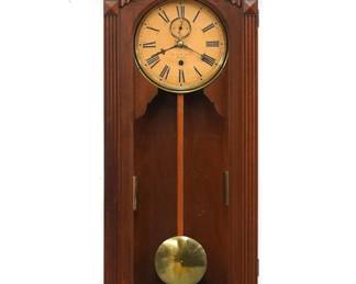 A late 19th century Gilbert No. 11 Regulator wall clock.  8-day dual weight driven time only movement with papered metal dial and Roman numerals, subsidiary seconds.  Walnut case with carved detail features a shaped crest above a single arched door with flat reeded pilasters above a shaped drop with inset Burl panel and carved detail.  Refinished with minor wear, re-papered dial, crack in right side glass, running when cataloged.  49 1/2" high.  ESTIMATE $600-800