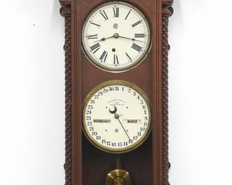 A late 19th century Waterbury No. 28 model wall clock.  8-day time only movement with painted metal dials and Roman numerals, lower calendar mechanism with apertures indicating day, month and date.  Walnut case with carved details and turned finials features a carved crown with turned crossbar over a single door with arched glass flanked by turned columns above a shaped bracket drop.  Older refinishing with minor wear, running when cataloged.  40 1/2" high.  ESTIMATE $200-400