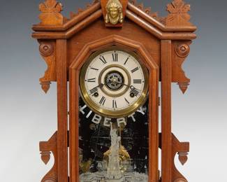 A turn of the century Ingraham Liberty model kitchen shelf clock.  8-day time, strike and alarm movement with papered metal dial and Roman numerals.  Walnut case with shaped crest and turned finial over a single door with clear dial glass and stenciled lower "Liberty" glass on a molded base.  Older refinishing with some wear, dial re-papered, stencil wear, running when cataloged.  23 3/4" high.  ESTIMATE $100-150 