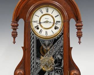 A late 19th century Gilbert Callia model shelf clock.  8-day time and strike movement with papered metal dial and Roman numerals.  Walnut case with carved crest and arched top above an arched door with stenciled glass in a molded frame flanked by drop finials on a plinth base.  Refinished with minor wear, re-papered dial, running when cataloged.  23 1/4" high.  ESTIMATE $100-150
