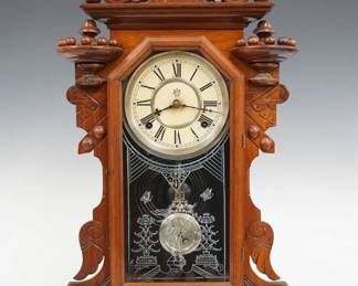 A turn of the century Waterbury Hudson model kitchen shelf clock.  8-day time and strike movement with papered metal dial and Roman numerals.  Walnut case with carved crest and turned finials over a molded door with stenciled glass, shaped sides and a carved molded base.  Paper label on back 50% intact.  Refinished with minor wear, dial discoloration, running when cataloged.  23" high.  ESTIMATE $100-150