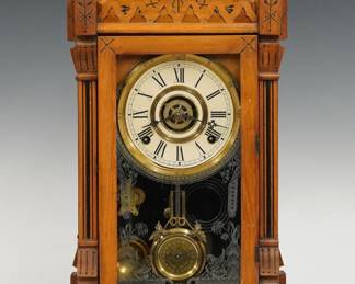 A 19th century Gilbert Dacca model Victorian shelf clock.  8-day time, strike and alarm movement with papered metal dial and Roman numerals.  Light Ash case with Ebonized with gallery top and turned finials above a door with stenciled glass, flanked by molded pilasters on a molded base.  Paper label on back 20%.  Original finish with some wear, some dial wear, running when cataloged.  21 1/2" high.  ESTIMATE $100-150