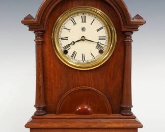 A turn of the century Waterbury arched top shelf clock.  8-day time and strike movement with papered metal dial and Roman numerals.  Walnut case with arched crest and turned pilasters over a single door and lower molded base.  Interior paper label 80% intact.  Older refinishing with minor wear, dial re-papered, running when cataloged.  14 1/2" high.  ESTIMATE $100-150 
