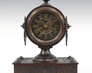 A turn of the century Ansonia Tucker No. 2 model cast iron desk clock.  30-hr time only movement with lever escapement, metal dial with Roman numerals.  Cast iron case with circular movement housing and drop handles on a lower base with faux drawer.  Original dark finish with wear, running when cataloged.  12" high.  ESTIMATE $100-150