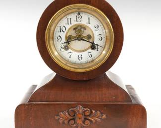 An early 20th century Waterbury Wales model shelf clock.  8-day time and strike movement with visible escapement, two part porcelain dial  and Arabic numerals.  Mahogany Balloon shape case with a molded Brass dial door and a simple molded base with applied carving and Brass feet.  Paper label underside 80% intact.  Refinished with minor wear, minor veneer damage, running when cataloged.  9 3/4" high.  ESTIMATE $100-150
