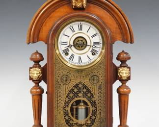 A late 19th century Ingraham Mascot model shelf clock.  8-day time, strike and alarm movement with papered metal dial and Roman numerals.  Walnut case with arched crest and turned finial with cast Liberty mask above an arched door with stenciled glass in a molded frame flanked by 3/4 columns with cast loin's masks on a molded base with inset level.  Paper label on back 50 % intact.  Refinished with minor wear, re-papered dial, running when cataloged.  22 1/2" high.  ESTIMATE $100-150