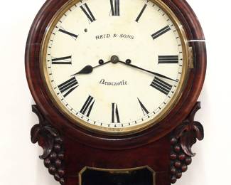 A mid 19th century English drop dial wall clock.  8-day double fusee movement with shouldered plates and painted Iron dial with Roman numerals marked "Reid & Sons, Newcastle".  Mahogany case with circular molded bezel and Brass dial door with carved vintage design side ears, Brass pendulum aperture molding and rounded bottom.  Older finish with some wear, shrinkage crack in bezel running when cataloged.  21 1/2" high.  ESTIMATE $400-600  NOTE: Reid & Sons were well known jewelers and silversmiths in the 19th century with stores in Newcastle and London.