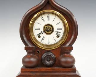 A late 19th century Ingraham Oriental Model shelf clock.  30-hr spring driven time, strike and alarm movement with papered metal dial and Roman numerals.  Molded Rosewood case with Gothic "Onion" top over a circular door with molded Brass bezel and a molded base.  Facsimile paper label verso.  Refinished with slight wear, re-papered dial, running when cataloged.  18" high.  ESTIMATE $200-300
