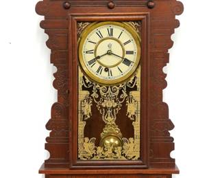 A turn of the century Gilbert Champlain model Kitchen wall clock.  8-day time only movement with papered metal dial and Roman numerals.  Walnut case with pressed design features a shaped crest over a molded door with stenciled glass above a shaped bracket drop.  Paper labels on back 70% intact.  Older refinishing with minor wear, re-papered dial, running when cataloged.  29 1/4" high.  ESTIMATE $100-150