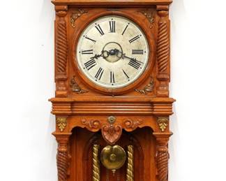 A late 19th century Waterbury Augusta model wall clock.  8-day weight driven time & strike movement with painted metal dial and Roman numerals.  Oak case with cast Brass ornamentation features an arched crown and central finial with cast dragons over a circular dial door flanked by spiral turned columns over an open well with paneled back, spiral columns and shaped drop.  Paper labels on back 80% intact.  Refinished with some wear, running when cataloged.  51 1/2" high overall. ESTIMATE $600-800