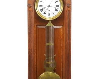 A turn of the century Ansonia Regulator No. 16 model wall clock.  8-day weight driven time only movement,  porcelain dial with Arabic numerals, sweep seconds and bi-metallic compensating pendulum.  Oak case with carved detail features a shaped stick and ball crest over an arched door with reeded detail and a scrolled bracket drop.  Older finish with minor wear, lacks side scrolls on drop, running when cataloged.  84" high overall.  ESTIMATE $2,000-3,000