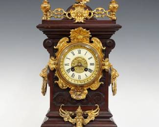 A late 19th century Lenzkirch Table clock.  8-day spring driven time and strike movement with porcelain dial, gilded cast center and Roman numerals, serial #751627 indicates a production date of 1886.  Walnut case with carved and molded detail features gilded cast Brass finials, appliques and gallery over a circular dial door with beveled glass, Lion's Mask side handles and Lion's Paw feet.  Older finish with minor wear, running when cataloged.  22" high overall. ESTIMATE $800-1,200