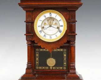 A 19th century E. N. Welch Khedive model Victorian shelf clock. 8-day time and strike movement with two part porcelain dial, visible escapement and Roman numerals, fancy pendulum with glass insert. Mahogany case with shaped top above a circular Brass bezel and open portico with stenciled glass, flanked by turned columns on a molded base. Refinished with minor wear, dial hairlines and small flake at 4:00, running when cataloged. 17 1/2" high. ESTIMATE $300-400