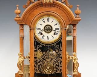 A late 19th century Ansonia Triumph model mirror side shelf clock.  8-day time, strike and alarm movement with papered metal dial and Roman numerals.  Oak case with turned finials features a carved arched crest with cast Liberty mask above an arched door with stenciled glass flanked by mirrored pilasters and original cast cherub figures on a rounded base.  Refinished with minor wear, re-papered dial, running when cataloged.  24 1/4" high.  ESTIMATE $200-300