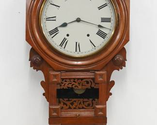 A late 19th century Anglo American schoolhouse clock.  New Haven 8-day time and strike movement with painted metal dial and Roman numerals.  Mahogany case with octagonal molded bezel and Brass dial door, over shaped ears, geometric moldings and a lower door with fretwork detail.  Paper label on back 60% intact.  Older refinishing with minor wear, re-painted dial, running when cataloged.  31" high.  ESTIMATE $200-300