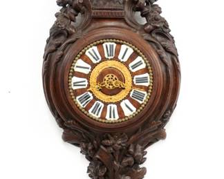 A 19th century Carved Black Forest Cartel clock.  8-day Kohler time and strike movement, wood dial with porcelain markers and Roman numerals, gilded floral inner ring and filigree hands.  Oak case with extensive hand carved detail features a flower basket crown with scrolled detail, foliate bezel and shaped drop with floral design.  Older finish with some wear, replaced movement, runs momentarily when cataloged.  29 1/2" high.  ESTIMATE $600-800