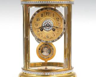 A turn of the century French crystal regulator by Samuel Marti, Paris, retailed by A. Stowell & Co., Boston.  8-day time and strike movement with gilded Brass dial and Arabic numerals, bezel and pendulum with inset brilliants at edges, dial with Champleve center, pendulum with portrait monogramed S. G.  Oval Brass case with inlaid Champleve detail features curved beveled glass on all four sides, on a molded base with bracket feet.  Minor wear on case and dial, some brilliants have darkened, running when cataloged.  11 1/2" high overall.  ESTIMATE $800-1,200