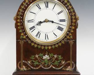 An early 19th century Regency Period Bracket clock.  8-day cable driven double fusee movement with shouldered plates and painted metal dial with Roman numerals.  Mahogany case with an arched top, Brass Lions mask side handles, molded dial door and ball feet, extensive inlaid detail in Brass, Mother-of-Pearl and enamel, Brass filigree side panels with fish scale design.  Older refinishing with minor wear, some repair and loss to inlay, restored dial, running when cataloged.  17 1/2" high overall.  ESTIMATE $600-800