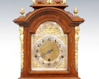 An early 20th century German Bracket clock.  8-day spring driven time and strike movement with quarter hour Westminster chimes, arched Silvered dial, gilded spandrels and Arabic numerals, serial #3027 marked "Patented in all Countries, Made in Wurttemberg".  Walnut case with a step molded top features gilded cast Brass finials, Carytid posts, side panels and appliques over an arched dial door with beveled glass, molded base and Brass paw feet.  Old finish with some wear, dial wear, lacks minute hand, wound tight when cataloged.  19 1/2" high overall.  ESTIMATE $200-300