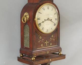 An early 19th century George IV Period Bracket clock by John Frodsham, London.  8-day cable driven double fusee movement with convex painted metal dial with Roman numerals marked "Frodsham, Gracechurch Street, London" with shouldered plates, additionally marked "Frodsham, Gracechurch Strt, London" on backplate.  Mahogany case with an arched platform top and Pineapple finial with inlaid Brass vine and flower detail, side handles, molded dial door and ball feet, flanked by Brass fish scale side panels, includes the original matching inlaid wall bracket.  Older refinishing with minor wear, some small veneer flakes, minor dial wear, running when cataloged.  28 3/4" high overall.  ESTIMATE $1,500-2,500