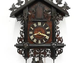 A turn of the century Black Forest Cuckoo wall clock.  8-day time and strike, three horn Trumpeter two weight movement with Brass cut-out plates and wooden dial with applied Roman numerals and filigree hands.  Walnut case with hand carved detail features a foliate crest on a body with molded posts and grape leaf detail with turned finials.  Older finish with original Ebonized detail, minor wear, one finial with glued repair, running when cataloged.  27" high plus weight drop.  ESTIMATE $800-1,200