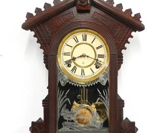 A turn of the century Gilbert Kitchen wall clock.  8-day time and strike movement with papered metal dial and Roman numerals.  Mixed wood case with turned finial on a pediment crest with Liberty mask over and arched door with stenciled glass and a shaped drop.  Facsimile paper label on back.  Original finish with some wear, running when cataloged.  25" high.  ESTIMATE $100-150