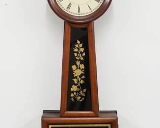 A mid 19th century Banjo clock attributed to George D. Hatch, North Attleboro, MA. 8-day weight driven time only movement with papered metal dial and Roman numerals, wooden pendulum stick with detachable Brass bob. Cherry case with circular dial door over a tapered throat and square lower door, both having reverse painted glasses with gilded detail. Refinished with minor wear, re-papered dial, running when cataloged. 29" high. ESTIMATE $400-600