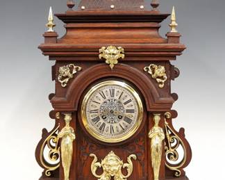 A late 19th century Lenzkirch Table clock.  8-day spring driven time and strike movement with Niello decorated  Silvered dial,  Roman numerals and fancy filigree hands, serial #999035 indicates a production date of 1893.  Oak case with molded detail features cast Brass finials, masks, appliques and scrollwork, arched molded crown over a circular open dial flanked by Neoclassical figural corner posts, cast side plated rear scrolls and a molded base with flattened bun feet.  Refinished with slight wear, minor case damage, minor dial wear, replaced Eagle finial, running when cataloged.  26 1/2" high overall. ESTIMATE $1,000-1,500