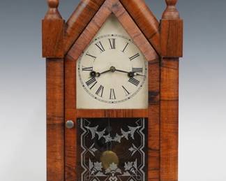 A turn of the century Waterbury steeple clock.  8-day time and strike movement with painted metal dial and Roman numerals.  Rosewood case with Gothic Arch crest and turned finials over a single door with clear dial glass and stenciled glass lower on a molded base.  Interior paper label 80% intact.  Older refinishing with some wear, dial wear, running when cataloged.  19 1/4" high.  ESTIMATE $100-150 