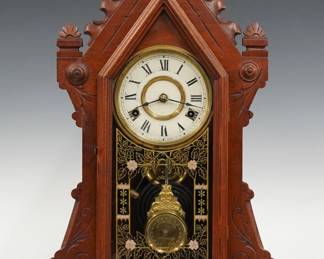 A late 19th century New Haven Clyde model shelf clock.  8-day time and strike movement with papered metal dial and Roman numerals.  Walnut case with carved pediment crest above a peaked door with painted and stenciled glass in a molded frame on a molded plinth base.  Paper label on back 80% intact.  Refinished with minor wear, dial wear, running when cataloged.  22 1/4" high.  ESTIMATE $100-150