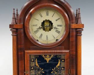 A mid 19th century American clock, retailed by Daniel Pratt & Son. 8-day time and strike movement with painted metal dial and Roman numerals.  Mahogany four column O. G. Gothic (Onion Top) case with single door, circular dial glass and reverse painted lower glass.  Older refinishing with some wear, dial wear, flakes to lower glass, small flakes to finials, replaced front and backboards, running when cataloged. 19 3/4" high. ESTIMATE $100-150