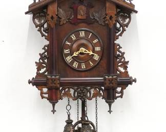 An early 20th century Black Forest style Cuckoo wall clock by the American Cuckoo Clock Co.  30-hr Brass time and strike two weight movement with wooden dial and applied Roman numerals.  Walnut case with hand carved detail features a foliate crest on a body with molded posts and grape vine detail with turned finials.  Paper label on back 60% intact.  Refinished with minor wear, running when cataloged.  23 1/2" high plus weight drop.  ESTIMATE $400-600