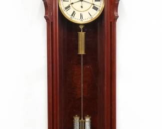 A late 20th century Seth Thomas replica No. 19 Railroad wall clock.  8-day weight driven time only movement with dead beat escapement and a 12" two part painted metal dial with Roman/Arabic numerals, sweep seconds and a two jar faux Mercury pendulum with steel rod.  Mahogany  case with carved detail features a shaped crest with carved fan and turned finials over a single arched door flanked by turned pilasters with scrolled capitols and bases over a lower shaped drop with turned finials.  Original finish with minor wear, running when cataloged.  75" high overall.  ESTIMATE $2,000-3,000