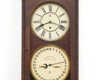 A late 19th century Waterbury No. 27 model wall clock.  8-day time only movement with painted metal dials and Roman numerals, lower calendar mechanism with apertures indicating day, month and date.  Oak case with carved details features a shaped crest and turned finials over a single door with molded frame above a shaped bracket drop with carved panel.  Paper labels on back and bottom 30% intact.  Original dark finish with some wear, running when cataloged.  44 1/4" high.  ESTIMATE $300-500