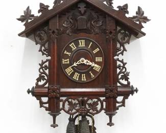 An early 20th century German Black Forest Cuckoo wall clock by Jos. Burger & Co., Schonach for Geo. Kuehl & Co, Chicago.  30-hr Brass time and strike two weight movement with wooden dial and applied Roman numerals.  Walnut case with hand carved detail features a foliate crest on a body with molded posts and grape leaf detail with turned finials.  Older finish with minor wear, running when cataloged.  25" high plus weight drop.  ESTIMATE $400-600