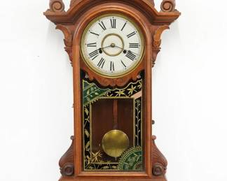 A late 19th century New Haven Regulator C C model mall clock.  8-day time and strike movement with painted metal dial and Roman numerals.  Eastlake Period Walnut case with carved detail and applied Lions masks, features a shaped crest with turned finials over an arched door with reverse painted glass flanked by shaped ears over a drop with shaped apron and turned finials.  Older refinishing with minor wear, dial crazing, running when cataloged.  40" high overall. ESTIMATE $400-600  