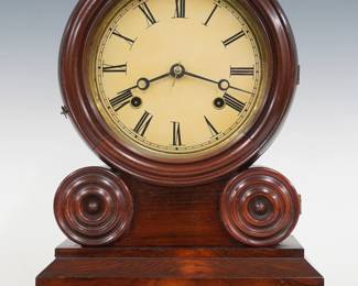 A late 19th century E. Ingraham Grecian model shelf clock. 30-hr time and strike movement with painted metal dial with Roman numerals.  Rosewood case with molded door and turned bosses, clear dial glass and simple molded base.  Paper label 60%.  Older refinishing with minor wear, re-painted dial, running when cataloged. 14 1/2" high. ESTIMATE $200-300