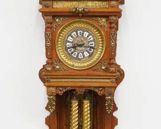 A late 20th century Oak wall clock, replica of an Ansonia "Antique Hanging" model. 8-day weight driven time & strike movement with embossed Brass dial, porcelain hour markers, and Roman numerals with cast pendulum bob. Oak case with extensive cast Brass ornamentation features a pediment crown with Neoclassical plaque and turned finials with metal arms over an open dial with cast spandrels flanked by squared columns over an open well with filigree brackets, cast back detail and shaped drop. Some wear, running when cataloged. 45 3/4" high overall. ESTIMATE $800-1,200