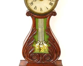 A mid 19th century Boston Area Lyre banjo clock with alarm.  8-day time and alarm movement with painted iron dial and Roman numerals.  Mahogany case with carved foliate detail features an Eagle finial and Bell over a molded Brass dial door with convex glass, shaped throat panel with reverse painted glass, lower door with reverse painted glass, over a shaped drop with finial.  Older finish with some wear, dial wear,  running when cataloged.  41 1/4" high overall.  ESTIMATE $2,000-3,000