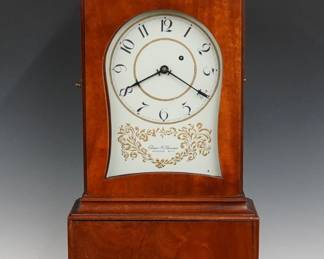 A late 20th century Elmer Stennes, replica Massachusetts shelf clock.  8-day weight driven time only movement with painted Iron dial and Arabic numerals, marked "Elmer O. Stennes, Weymouth, Mass" with a painted Bee lower right.  Mahogany Federal style case with pierced fretwork crest below a Brass Eagle finial, molded crown over an arched dial door in the hood section, body with an Inlaid Eagle medallion over a shaped skirt and flared French feet.  Original finish with minor wear, repairs to the crest and base edges, running when cataloged.  39 1/2" high.  ESTIMATE $1,500-2,500  