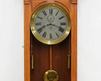  A late 19th century Waterbury No. 17 Regulator wall clock.  8-day dual weight driven time only movement with Graham dead beat escapement and maintaining power, 16" Silvered dial with Roman numerals, subsidiary seconds.  Oak case with broken arch top and turned finial above a single arched door with flat reeded pilasters above a shaped bracket drop with carved detail.  Older refinishing with minor wear, running when cataloged.  55 1/2" high.  ESTIMATE $1,000-2,000